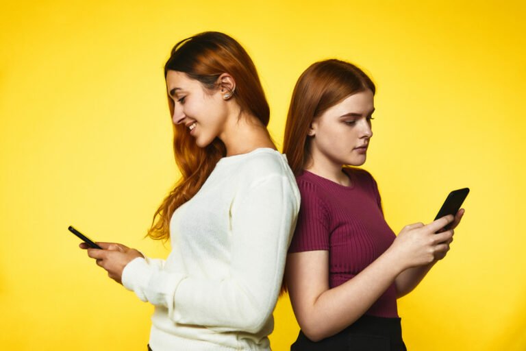 two young girls stand back back look their phones standing